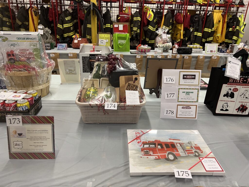 gift baskets and painted photo of a fire truck lined up in from of fire gear hanging in the background