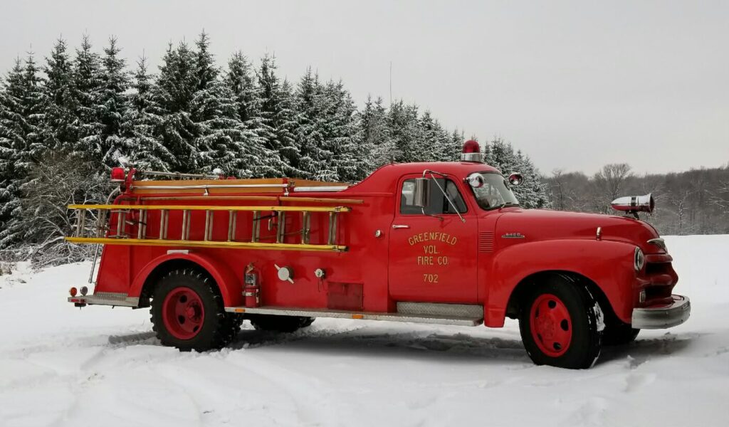 a red antique fire truck in the snow, with pine trees in the background