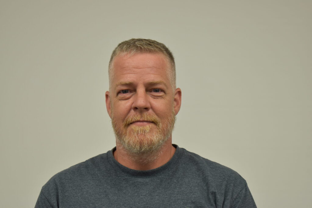 Man in grey shirt with short hair a goatee and mustache