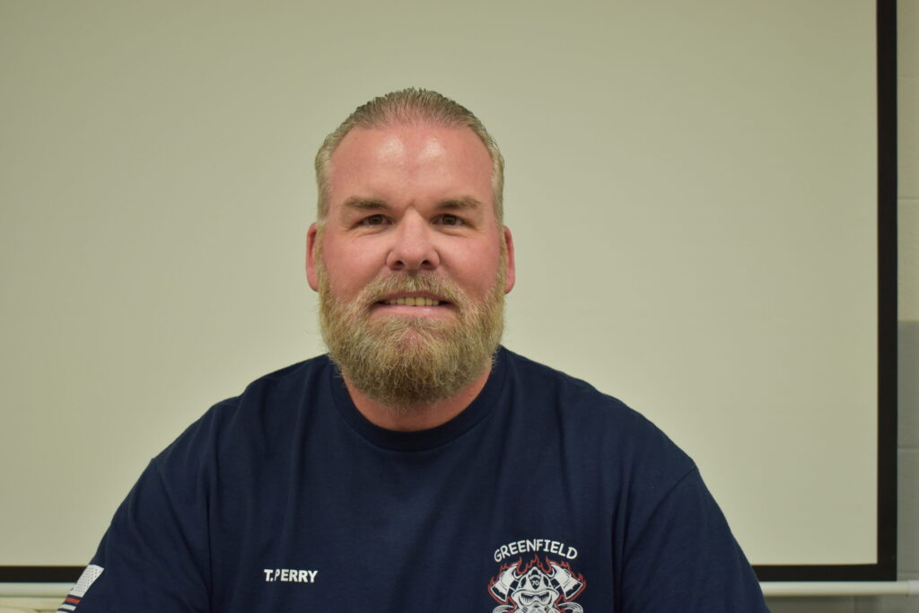 man in a blue shirt, hair pulled back a mustache and a beard