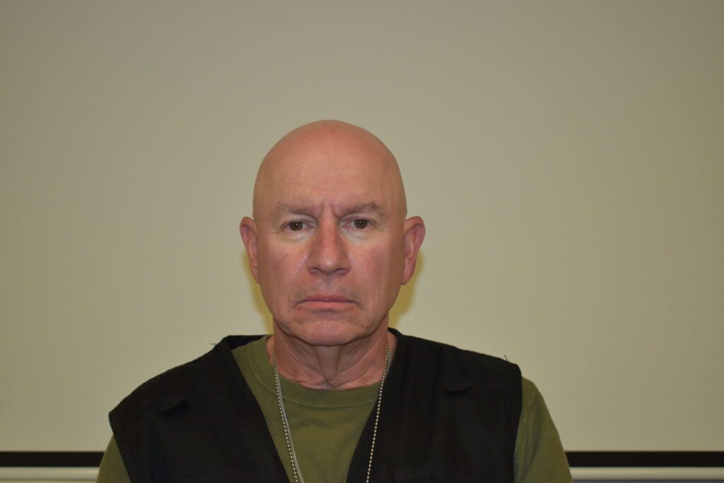bald man in green shirt with black vest