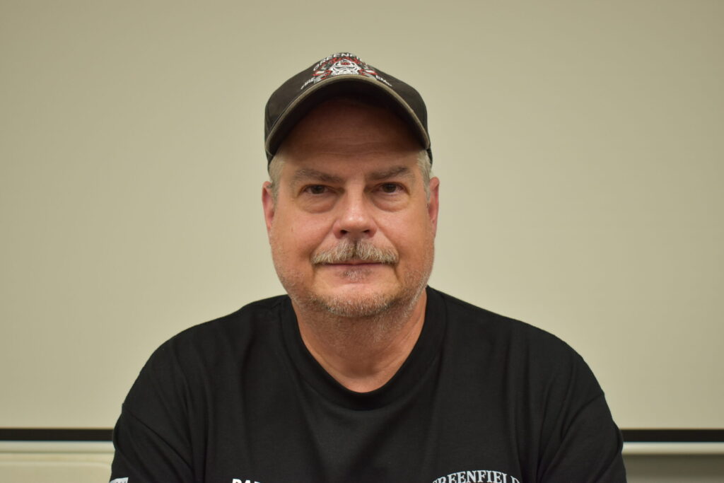 man in black shirt with a goatee and mustache, wearing a baseball cap