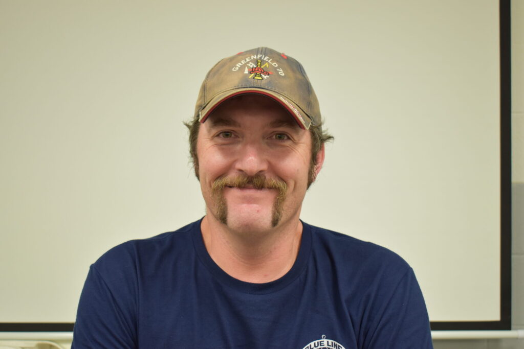 man with blue shirt, grey hat and a handle bar mustache