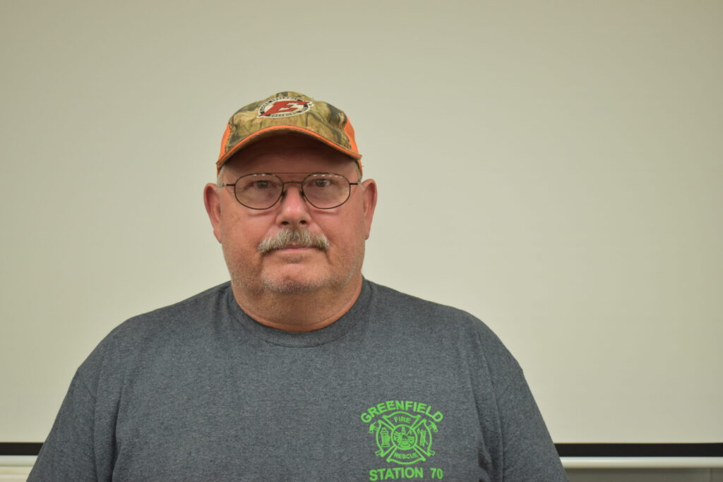 Man withe grey shirt, orange and tan baseball hat, glasses and mustache