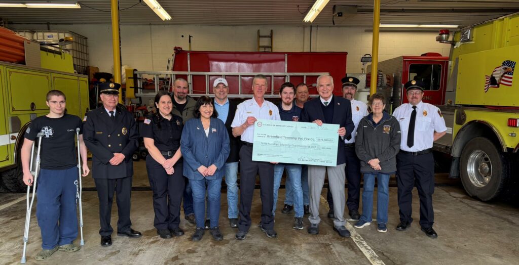 Group of people standing in a room holding a large check